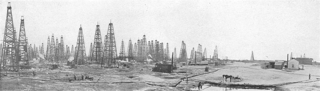 Historical photograph of an early 20th-century oil field with numerous derricks.